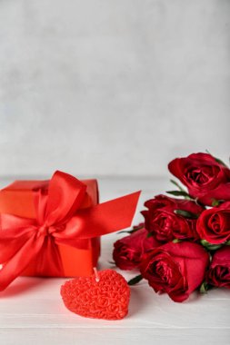 Candle, gift box and beautiful rose flowers on light wooden table, closeup. Valentine's Day celebration