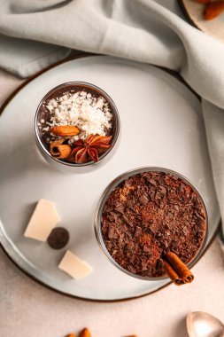 Plate with glasses of delicious chocolate pudding, coconut shavings, cinnamon and anise on white table