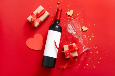 Composition with bottle of wine, glass and gifts on red background. Valentines Day celebration
