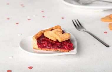 Heart-shaped plate with piece of sweet strawberry pie and cookie hearts for Valentine's day on white table
