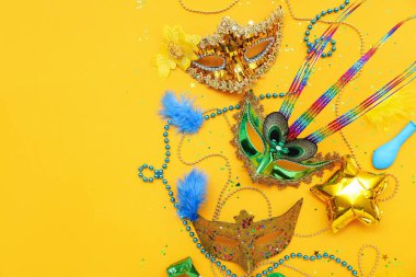 Carnival masks with beads, confetti and balloons on yellow background