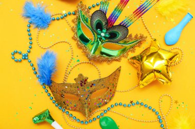 Carnival masks with beads, confetti and balloons on yellow background