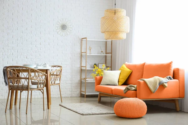 Stylish interior of living room with orange sofa, pouf and dining table