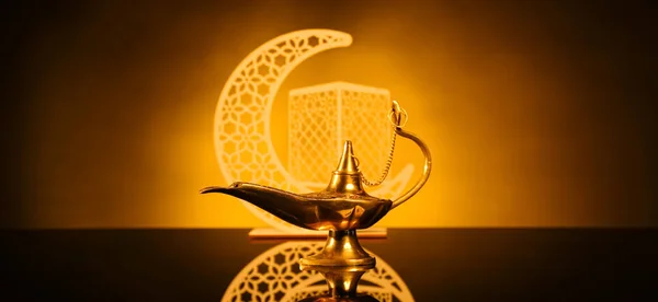 Aladdin lamp of wishes and decorative crescent on table against dark yellow background