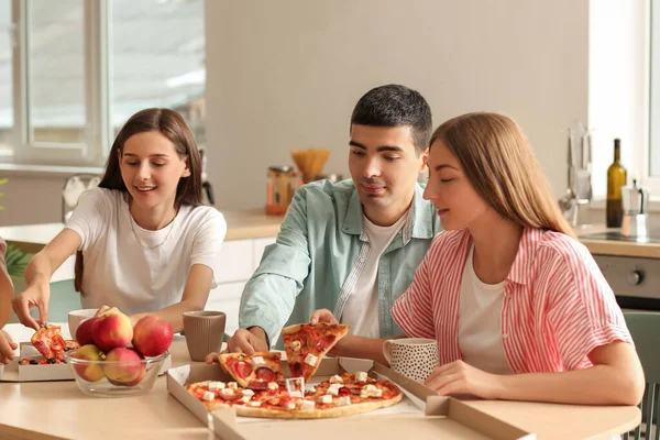 Group of friends eating pizza at table in kitchen