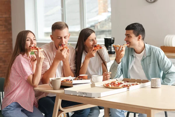Group of friends eating tasty pizza at table in kitchen
