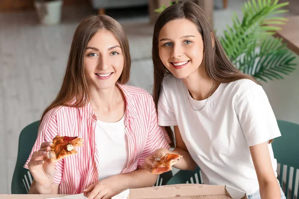 Female friends eating pizza at table in kitchen