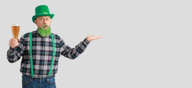 Elinde bir bardak birayla arka planda bir şey gösteren komik olgun bir adam. Aziz Patrick Günü kutlaması