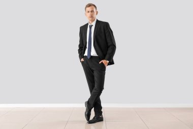 Handsome businessman in suit near light wall