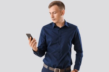 Young businessman in blue shirt using mobile phone on light background