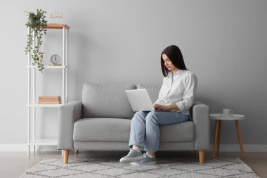 Evde kanepede dizüstü bilgisayar kullanan genç kadın