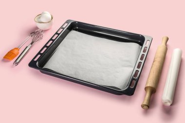 Baking tray with eggs and utensils on pink background