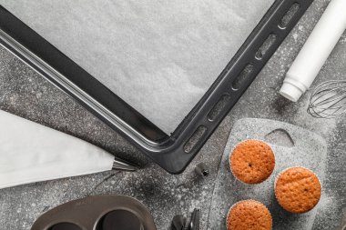 Baking trays with muffins and utensils on grunge background