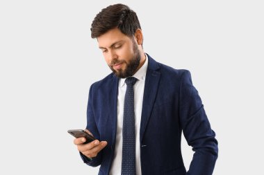 Young businessman using mobile phone on light background
