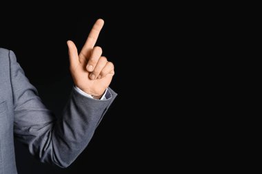 Young businessman pointing at something on black background, closeup