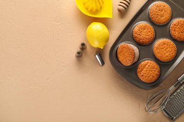 Tray with tasty muffins, lemon and utensils on color background