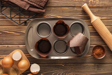 Muffin tray, rolling pin, eggs and cocoa powder on wooden background