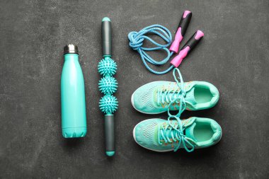 Skipping rope with sneakers, massage roller and bottle on dark background