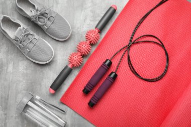 Skipping rope with mat, massage roller, sneakers and bottle on grunge background