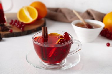 Glass cup of fruit tea with red currant and cinnamon on light background, closeup
