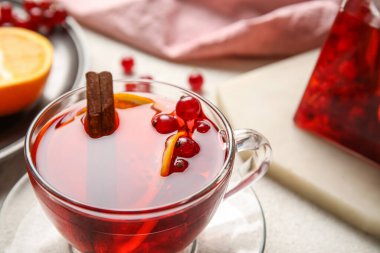 Glass cup of fruit tea with red currant and cinnamon on light background, closeup