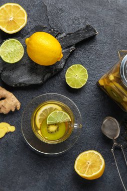 Glass cup of fruit tea with kiwi, lemon, lime and ginger on dark background
