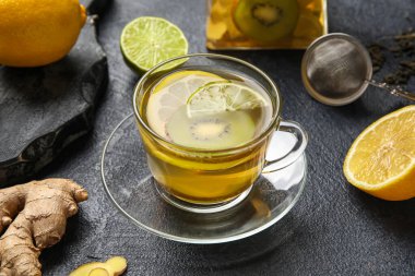 Glass cup of fruit tea with kiwi, lemon, lime and ginger on dark background, closeup
