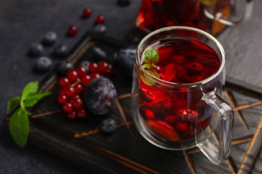 Board with glass cup of fruit tea and berries on dark background, closeup