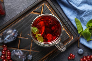 Board with glass cup of fruit tea and berries on dark background, closeup