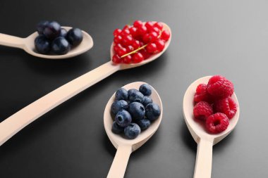 Wooden spoons with fresh berries on dark background, closeup