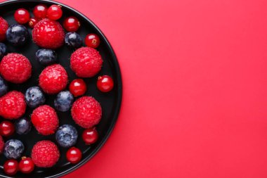 Plate of fresh berries on red background