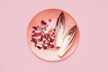 Plate with cut fresh endive on pink background