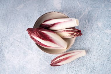 Bowl with bunches of fresh red endive on light background