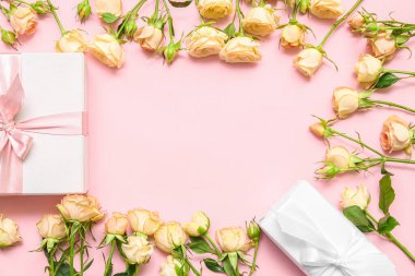 Frame made of beautiful rose flowers and gift boxes on color background