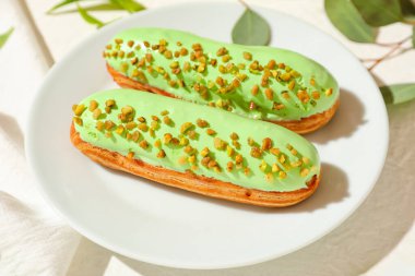 Plate with delicious eclairs on light background