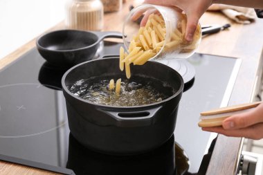 Woman pouring raw pasta into pot with boiling water on stove