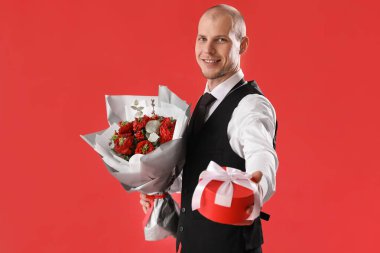 Young man with gift and bouquet of flowers on red background. Valentine's Day celebration