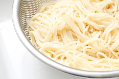 Colander with boiled pasta on light background, closeup