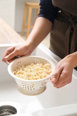 Woman holding colander with boiled pasta over sink, closeup