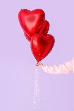 Woman with heart shaped balloons for Valentine's Day on lilac background