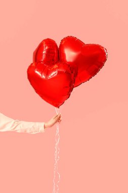 Woman with heart-shaped balloons for Valentine's Day on pink background