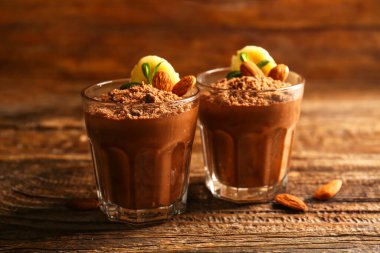Glasses with delicious chocolate pudding, almond, banana and mint leaves on wooden background