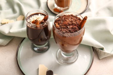 Plate with glasses of delicious chocolate pudding, coconut shavings, cinnamon and anise on white table