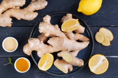 Plate with ginger roots, slices, lemon pieces and honey on dark wooden background