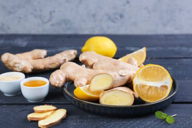 Plate with ginger roots, slices, lemon and bowl of honey on table