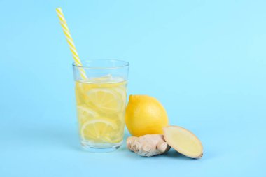 Fresh cut ginger, glass of water and lemon on blue background