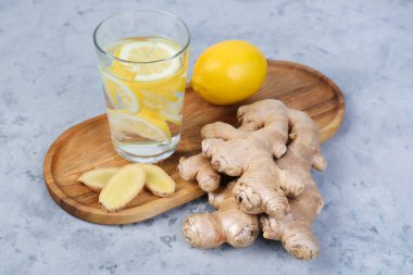 Cutting board with fresh ginger roots, slices, lemon and glass of water on grunge background