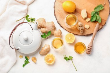 Composition with teapot, cup of tea, ginger, honey and lemon on light background