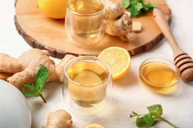 Wooden board with cup of tea, lemon, ginger and mint on light background