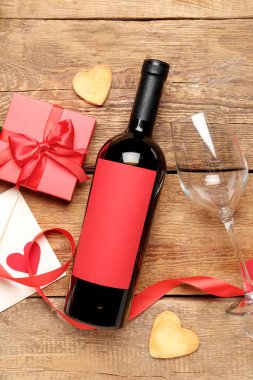Bottle of wine, gift box, glass and heart-shaped cookies on wooden background. Valentine's Day celebration